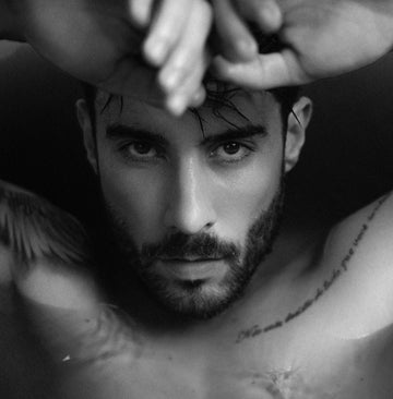 Black and white photo of a shirtless man with tattoos on his chest.